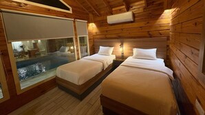 Una cabaña con dos camas, interior de madera y una pared de vidrio con vista a una piscina.