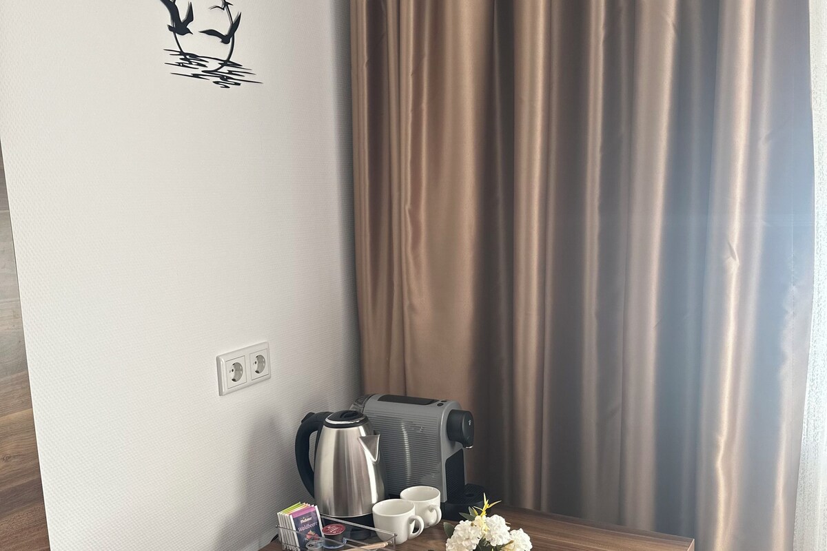 Una habitación pequeña con una mesa de madera, una tetera, dos tazas, un arreglo floral y un adhesivo en la pared.