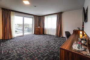 A hotel room with a large window, a wooden desk, a chair, and a television mounted on the wall. - Zenith Hotel Frankfurt Airport  (Kelsterbach)