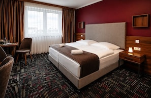 A hotel room with a bed, a desk, a chair, a nightstand, and a window with curtains. - Zenith Hotel Frankfurt Airport  (Kelsterbach)