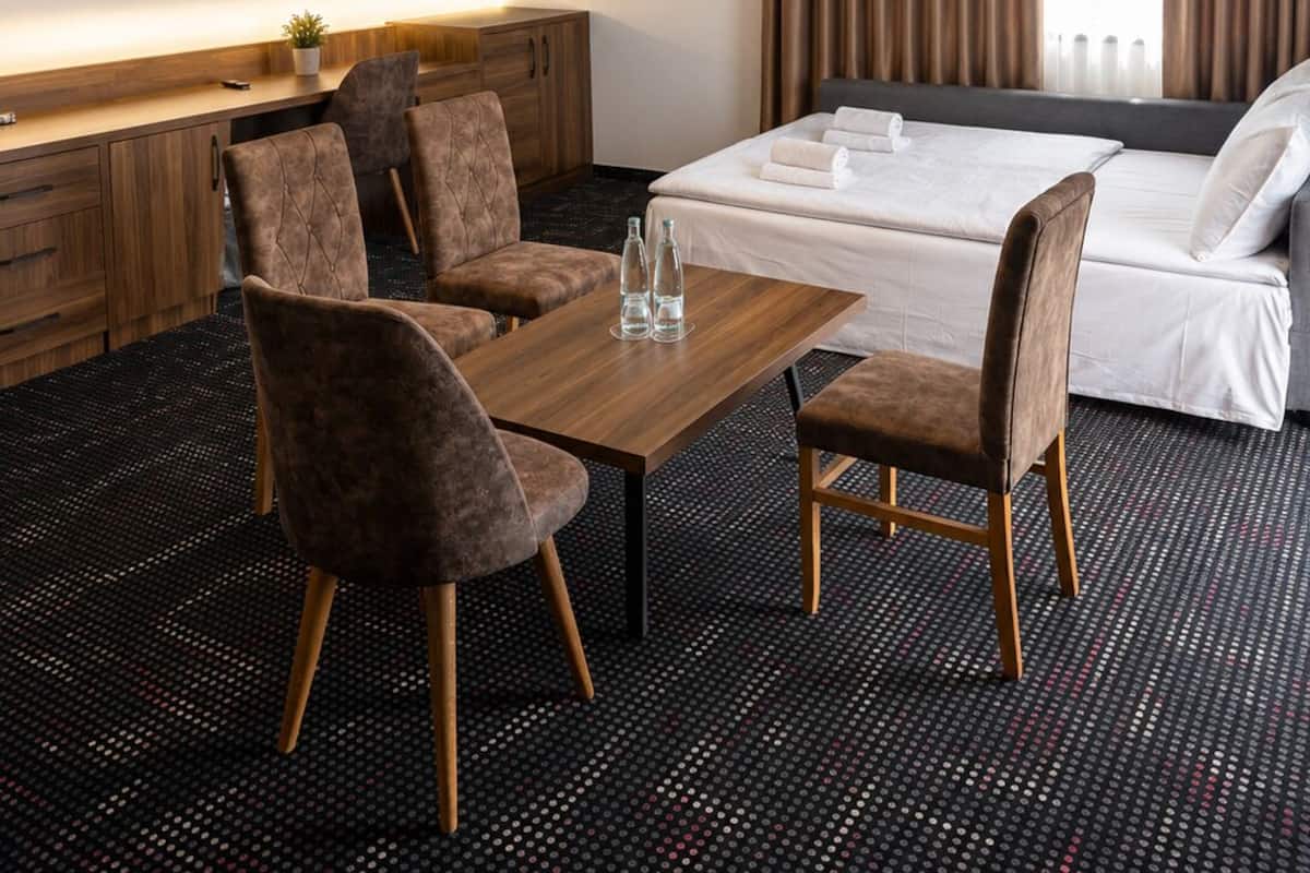 Ein Hotelzimmer mit einem Bett, einem Schreibtisch mit Flachbildfernseher, zwei Stühlen, einem Tisch und einem gemusterten Teppich.