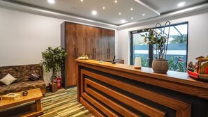 A modern reception area with a wooden counter, a sofa, a coffee table, and a large window with a view. - Zenith Hotel Frankfurt Airport  (Kelsterbach)