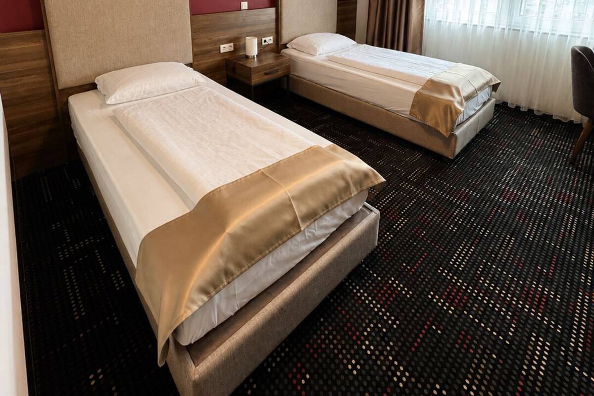 A hotel room with two beds, a desk, a chair, a window with curtains, and a red wall.