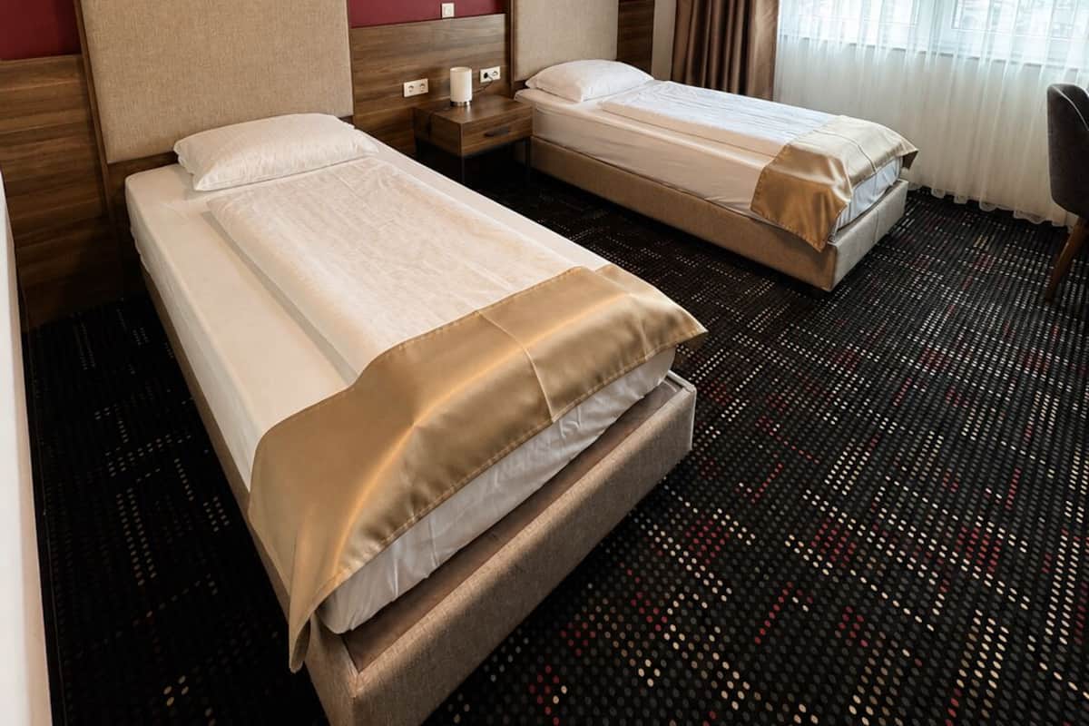 Ein Hotelzimmer mit zwei Betten, einem Schreibtisch, einem Stuhl, einem Fenster mit Vorhängen und einer roten Wand.