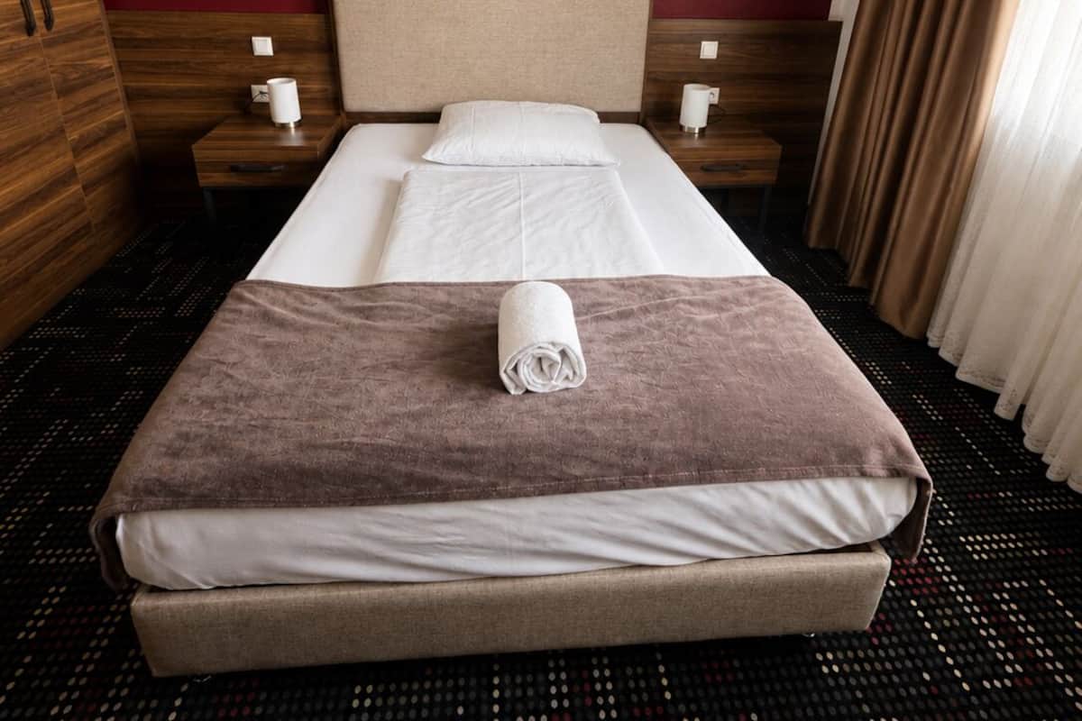 Ein Hotelzimmer mit einem Bett, einem Holzschrank, zwei Nachttischen und einem gemusterten Teppich.