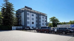 A modern hotel building with a clear sky, paved parking area, and a sign indicating a parking space. - Zenith Hotel Frankfurt Airport  (Kelsterbach)