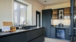 A modern kitchen with a large island, a built-in wine fridge, and a window with blinds. - The Luxury Harrogate Penthouse (North Yorkshire)