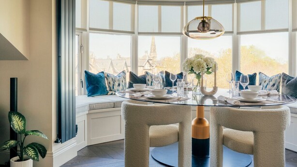 A dining area with a round table, chairs, and a view of a tower through large windows. - The Luxury Harrogate Penthouse (North Yorkshire)