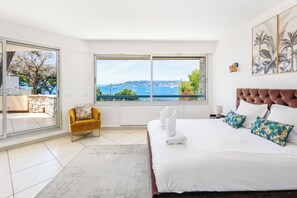 Un dormitorio con una cama grande, vistas al mar, una silla y un balcón.
