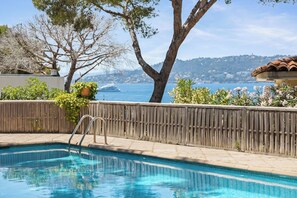 Una piscina con una valla de madera, un árbol y vista al mar.
