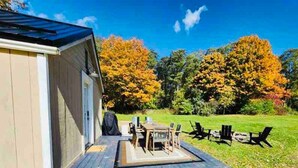 A covered patio area with a table and chairs, a covered grill, and a view of a grassy yard with trees. - Finger Lakes Renovated Farmhouse + Maple Farm! (Montour Falls)