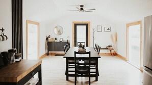 A spacious dining area with a long table, chairs, a ceiling fan, and a view through a door. - Finger Lakes Renovated Farmhouse + Maple Farm! (Montour Falls)