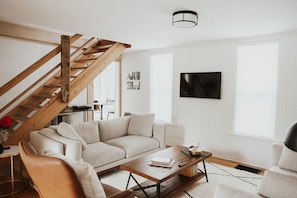 Una sala de estar moderna con una escalera de madera, un sofá, una mesa de centro y un televisor montado en la pared.
