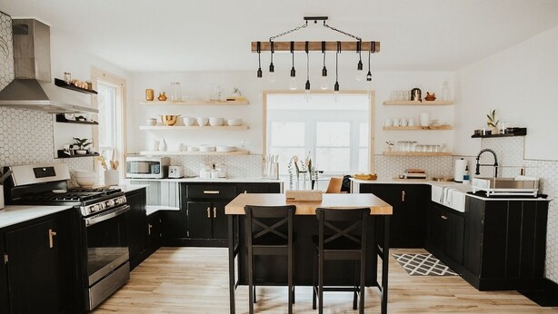 A modern kitchen with black cabinets, a wooden dining table, and a hanging light fixture. - Finger Lakes Renovated Farmhouse + Maple Farm! (Montour Falls)