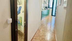 Un couloir avec une porte donnant sur une pièce, un coin cuisine avec des meubles verts et un sol carrelé.