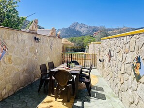 A stone-walled outdoor dining area with a table and chairs, a thatched roof, and a mountain view.