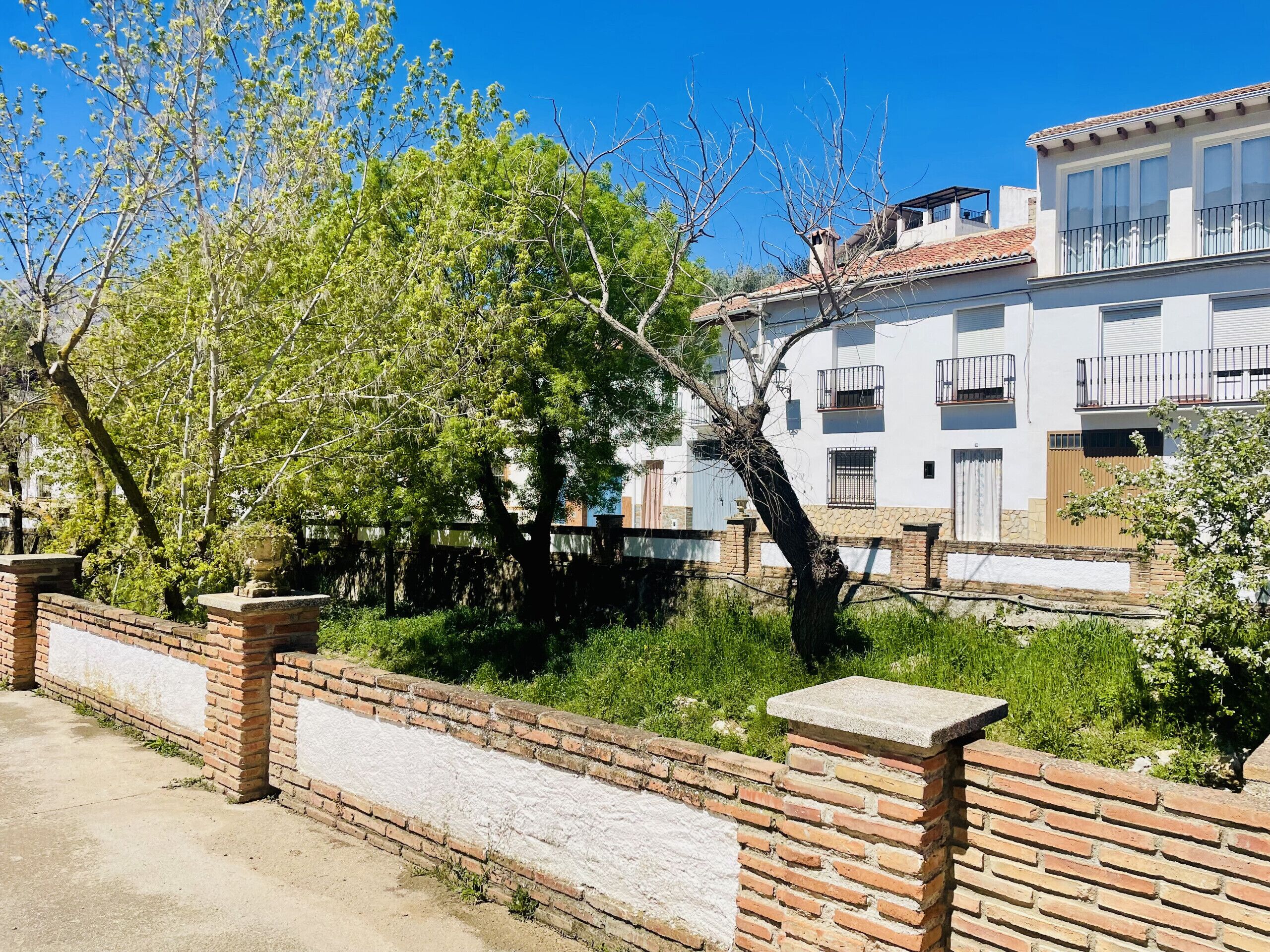 Un barrio residencial con un edificio blanco, muros de ladrillo y árboles.
