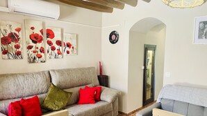 Un salon avec un canapé gris, des coussins rouges et verts, une chaise en bois et un autre canapé gris placé dans un coin.