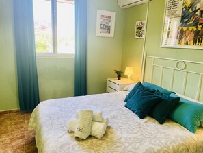 A hotel room with a bed, a nightstand, a lamp, a window with curtains, and a poster on the wall.