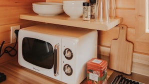 Une cuisine compacte équipée d’un four à micro-ondes, d’étagères contenant de la vaisselle et des verres, ainsi que d’une planche à découper.