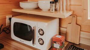 Une cuisine compacte équipée d’un four à micro-ondes, d’étagères contenant de la vaisselle et des verres, ainsi que d’une planche à découper.
