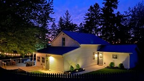 A two-story house with a deck, a fenced yard, and string lights. - 1875 Renovated Schoolhouse in the Finger Lakes with an Igloo! (Burdett)