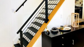 A staircase with black railings and wooden steps, leading to a black dresser with drawers and a small table with decorative items. - 1875 Renovated Schoolhouse in the Finger Lakes with an Igloo! (Burdett)