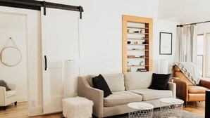 A modern living room with a sofa, a small stool, a round coffee table, a bookshelf, and a sliding door. - 1875 Renovated Schoolhouse in the Finger Lakes with an Igloo! (Burdett)