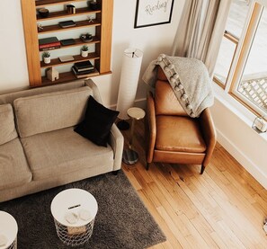 Un salon chaleureux avec un canapé, un fauteuil, une petite table d’appoint, une table basse ronde et une bibliothèque.