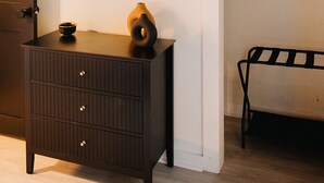 Una habitación con un aparador de madera oscura, un espejo redondo, un banco y una repisa con plantas.