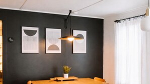 Un comedor con una mesa de madera y bancos, una pared negra con obras de arte enmarcadas y una lámpara colgante.