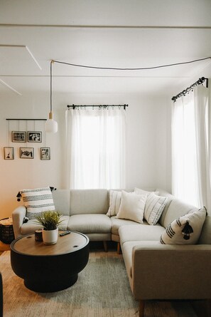 Moderni olohuone, jossa on kulmasohva, pyöreä sohvapöytä, riippuvalaisin ja verhotanko.