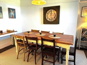 A dining area with a wooden table, six chairs, woven placemats, a wall clock, and framed artwork. - Glanrafon (Llwyngwril)