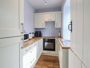 A compact kitchen with white cabinets, a microwave, a coffee maker, and an oven. - Glanrafon (Llwyngwril)