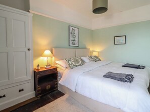 A bedroom with a bed, bedside lamps, a nightstand, a dresser, and artwork on the walls. - Glanrafon (Llwyngwril)