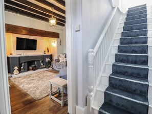 A staircase with dark carpeting and white balusters, leading to a living room with a fireplace, a television, and a sofa. - Glanrafon (Llwyngwril)