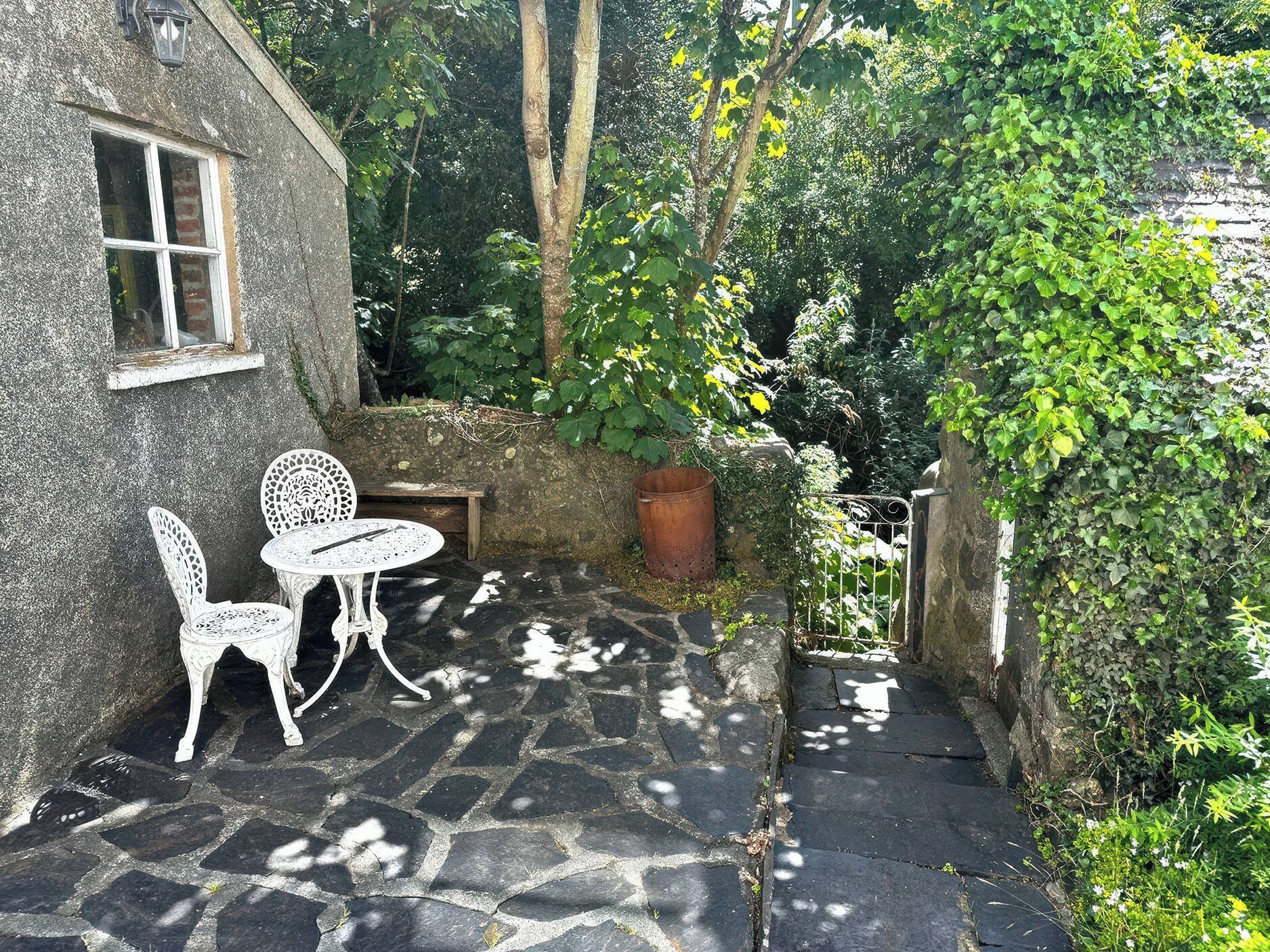 A stone patio with a table and chairs, a small window, and a stone wall.