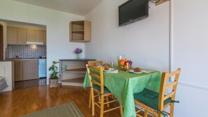 A compact kitchen with wooden cabinets, a dining table with chairs, a TV mounted on the wall, and a small plant on the counter. - Very nice studio apartment with sea view, balcony & parking space (Crikvenica)