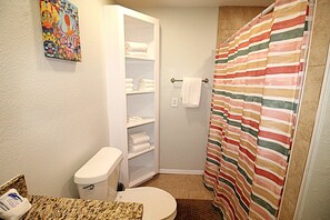 A bathroom with a toilet, a shower curtain, a towel rack, and a shelf with folded towels. - Newly remodeled home where the wildlife roam! (Port Mansfield)