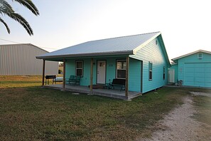 A single-story house with a porch, numbered 218, featuring a metal roof and a small front yard. - Newly remodeled home where the wildlife roam! (Port Mansfield)