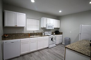 A kitchen with white cabinets, a microwave, a stove, a sink, and a trash can. - Newly remodeled home where the wildlife roam! (Port Mansfield)