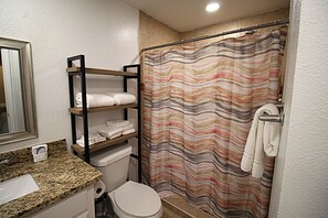 Ein Badezimmer mit Granitwaschtisch, Toilette, Dusche mit Streifenvorhang und Handtuchhalter.
