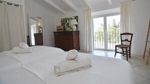 Una camera d'albergo con un letto grande, una cassettiera in legno, una sedia e un balcone con vista.