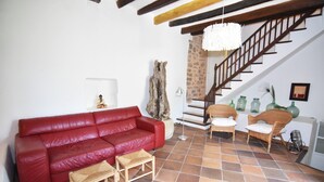 Un soggiorno con un divano in pelle rossa, una panca di legno, poltrone in vimini, una scala e un lampadario.