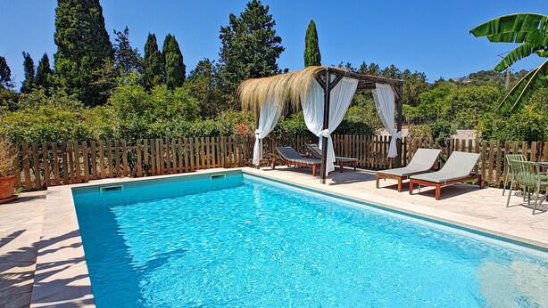 Una piscina rettangolare con una terrazza in legno, poltrone a sdraio, un ombrellone e una recinzione in legno.