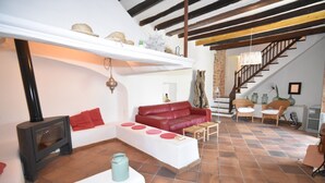Un soggiorno con camino, divano in pelle rossa, tavolino da caffè bianco e una scala che conduce a un piano superiore.