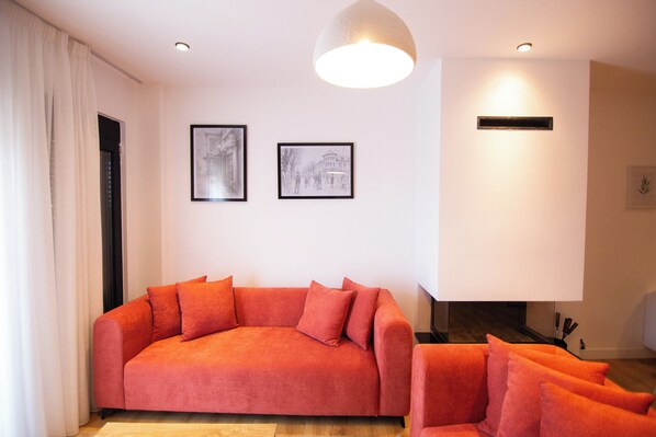 Un salon moderne avec un canapé rouge, deux tableaux encadrés au mur, un luminaire au plafond et une cheminée.