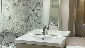 Un baño con pared revestida de mármol, lavamanos doble, inodoro y zona de ducha.