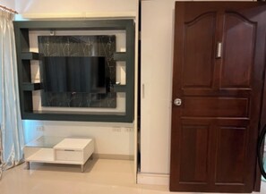 A room with a television mounted on a wall, a wooden door, and a white cabinet. - Spacious 42m2 condo in the middle of Jomtien, Pattaya full equipped (Muang Pattaya)
