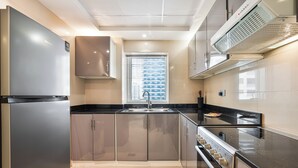 A modern kitchen with stainless steel appliances, a window with blinds, and a ventilation hood. - PVH - 2BR near Marina Promenade (Dubai)